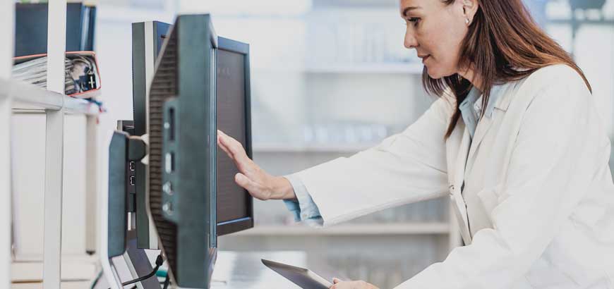 A female healthcare worker sits at her desk and points to her computer monitor<br>  