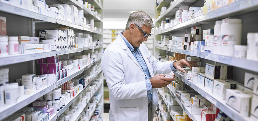 A pharmacist reads pill bottles in the back area of the pharmacy.