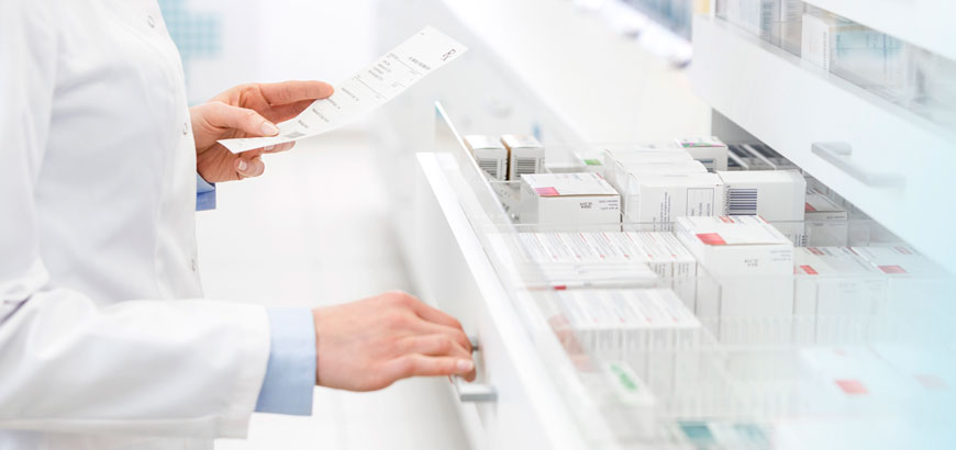 Close up of a pharmacist's hands as they open a drawer full of medication and hold a piece of paper in their other hand.