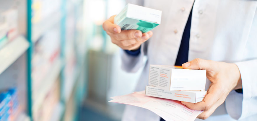 Close up of a pharmacist's hands holding prescription medication packaging.