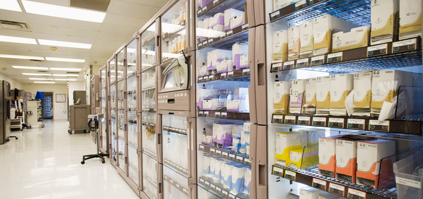 Behind the desk at a pharmacy, several bottles of medication are on shelves with glass doors