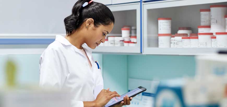A female pharmacist uses a tablet behind the pharmacy counter