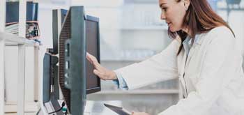 A female pharmacist looks at double computer monitors