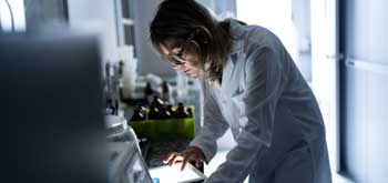 A pharmacist looks down at a tablet that shines on her face in an otherwise dark room