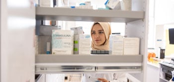 A female pharmacist wearing a hijab looks through medications on shelves