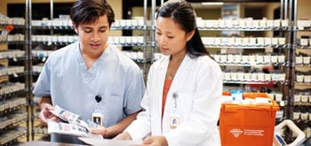 Two pharmacists look at paperwork behind the counter