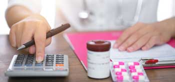 Close up of hands using a calculator with a pill bottle nearby<br>  