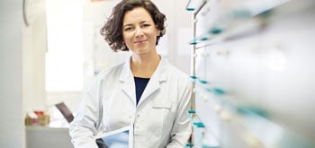 Sabrina Pugliese leans against a wall while wearing a lab coat