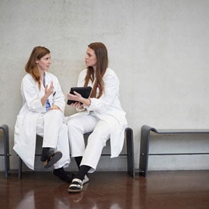 Two physicians sit together and talk in a hospital hallway<br>  