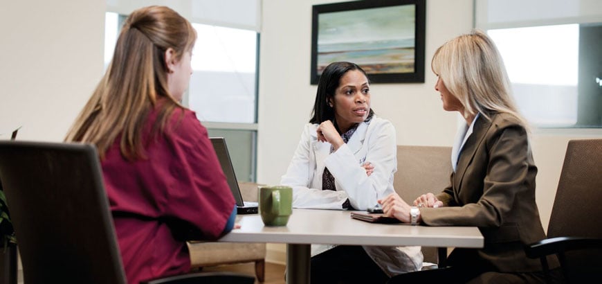 Healthcare workers sit and have a conversation at a large conference room table.<br>  