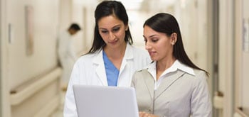 Two healthcare workers stand and look at a tablet together