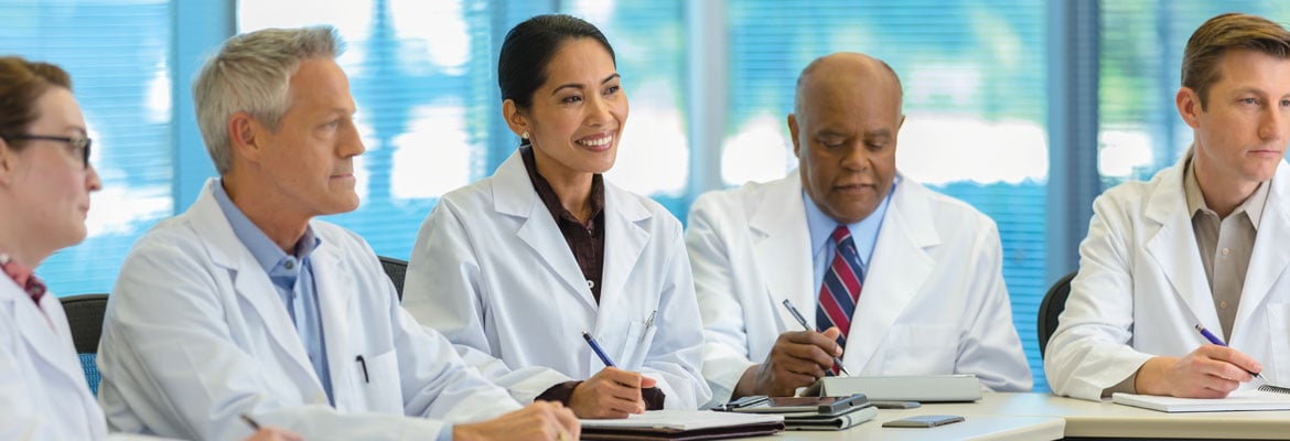 Five medical professionals sit at a conference table for a meeting