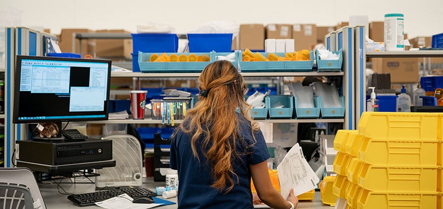 A pharmacy technician standing near a computer workstation filling prescription drug orders