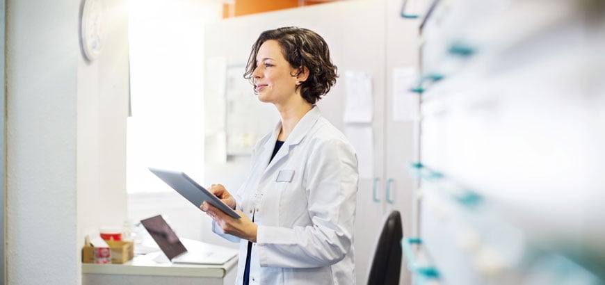 A female pharmacist stands among the shelves behind the pharmacy counter