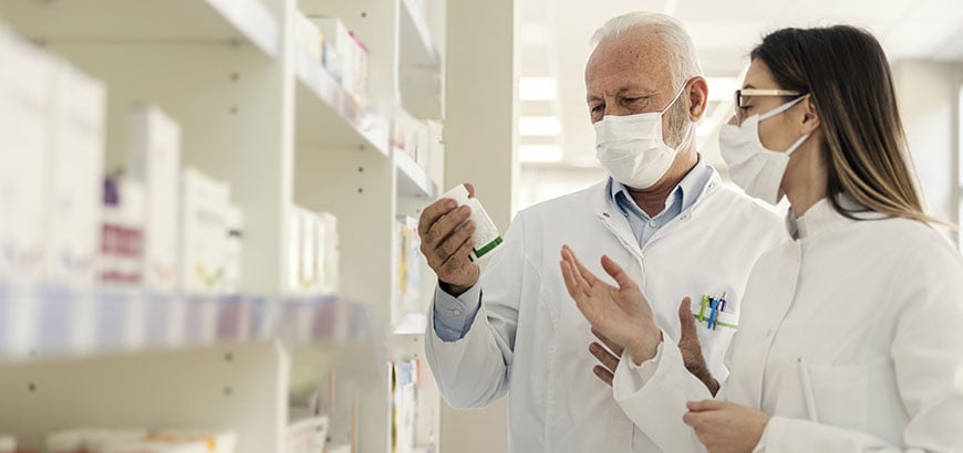 A male and female pharmacist wearing masks looking at a prescription pill bottle