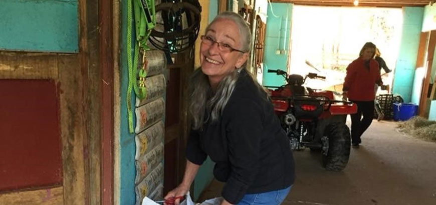 A woman in a horse stable smiling at the camera