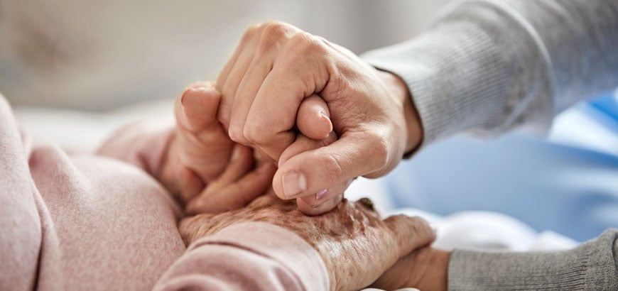 Close up of two elderly people holding hands while in a hospital bed.