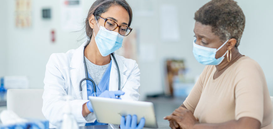 A doctor and a patient wearing masks and looking at a tablet