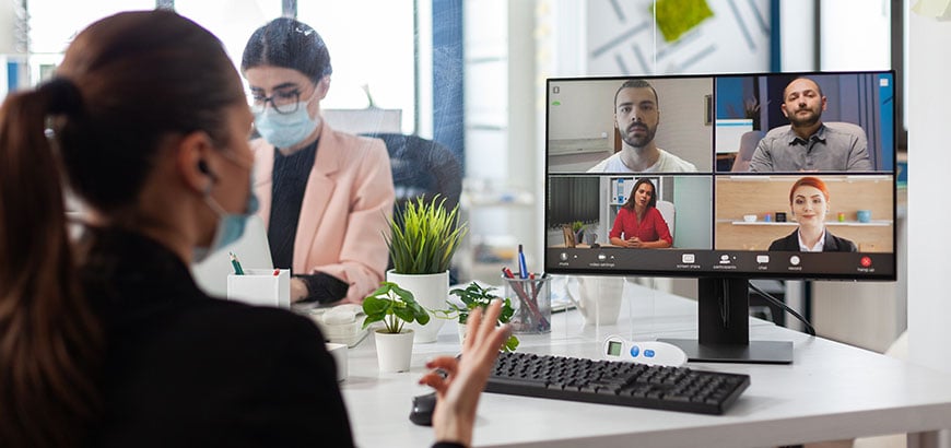 A person sitting in front of a computer monitor attending a virtual video conference