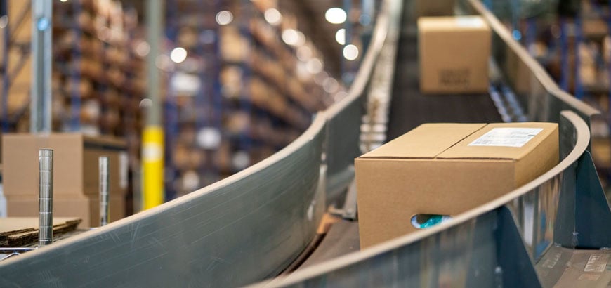 Two cardboard box packages slide down a conveyor belt inside a distribution center.