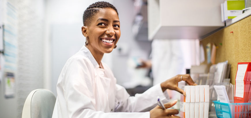 A pharmacist at a desk sorting prescription pill boxes.