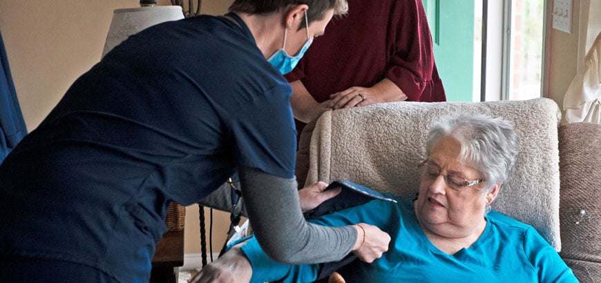 A home nurse checks an elderly patient's blood pressure as she sits in an armchair.