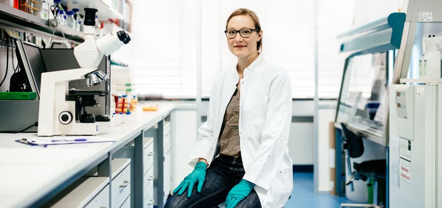 Scientist sits in a lab, there is a microscope on the table