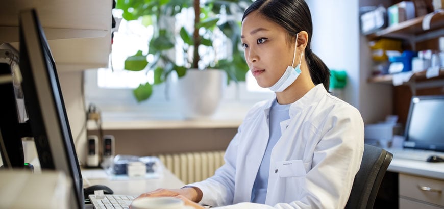 A female pharmacist sits at a computer while working in a pharmacist laboratory