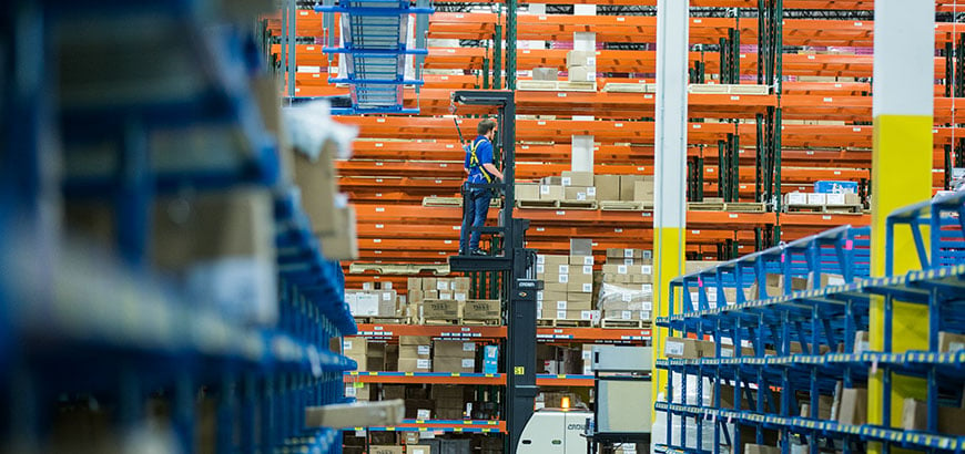 A worker standing on a forklift in a warehouse