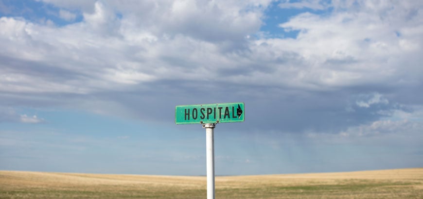 A sign that reads &quot;Hospital&quot; stands alone on a desert road