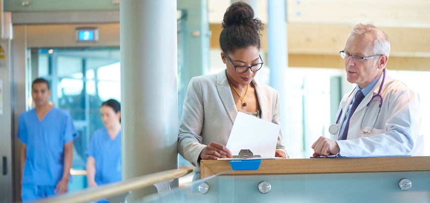 Two hospital executives discussing paperwork in a busy hospital hallway