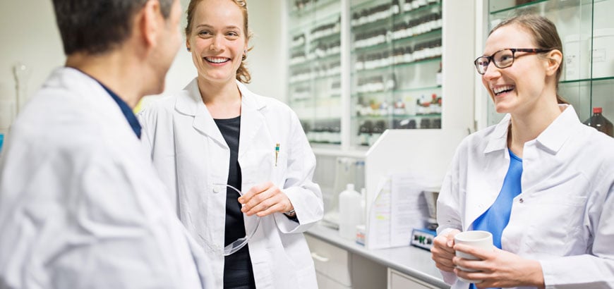 Three pharmacists smile together behind the pharmacy counter