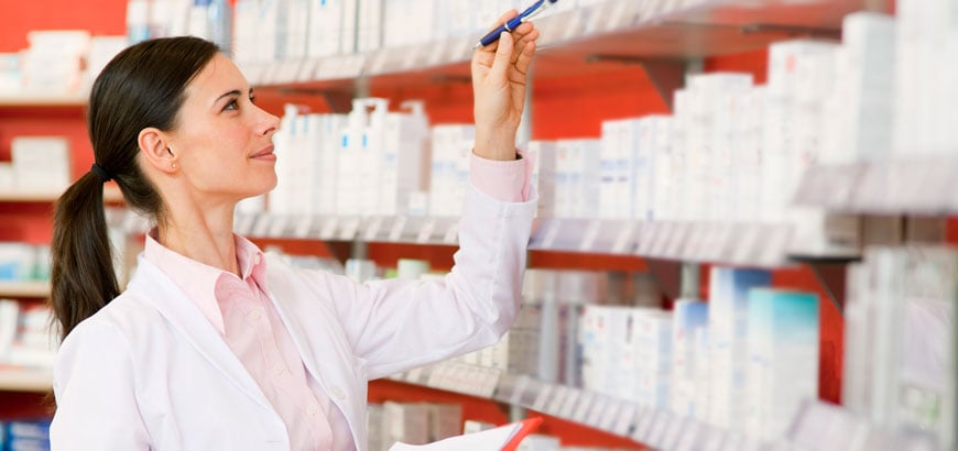 A pharmacist holding a pen and clipboard does inventory