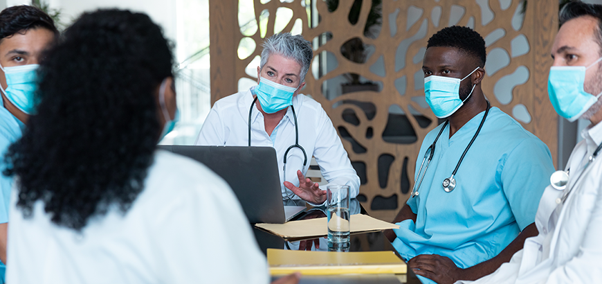 A group of doctors wearing masks sitting at a conference table