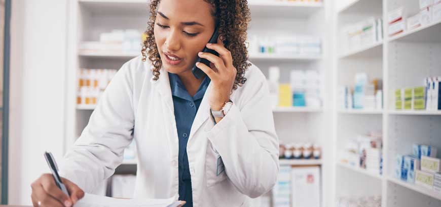 A female healthcare worker is on the telephone with one hand and using a pen to write notes on paper with the other hand.