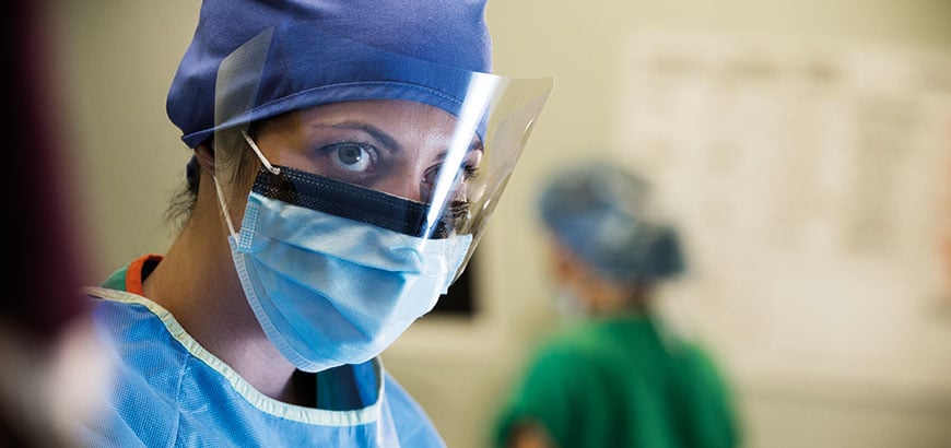 A healthcare worker in scrubs wearing a mask and faceshield