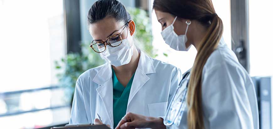 Two doctors wearing masks reviewing data on a clipboard