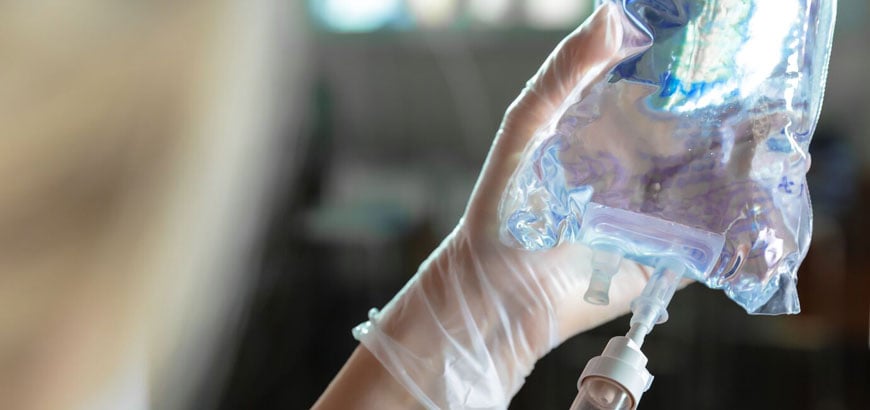 A gloved hand holding an IV bag