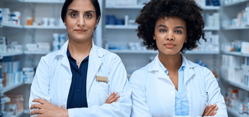 Two female pharmacists stand next to each other and cross their arms