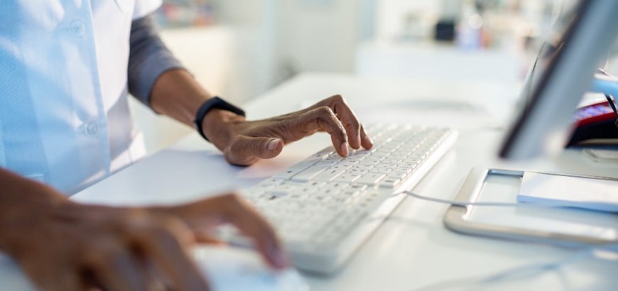 Partial view of person in white coat at a computer