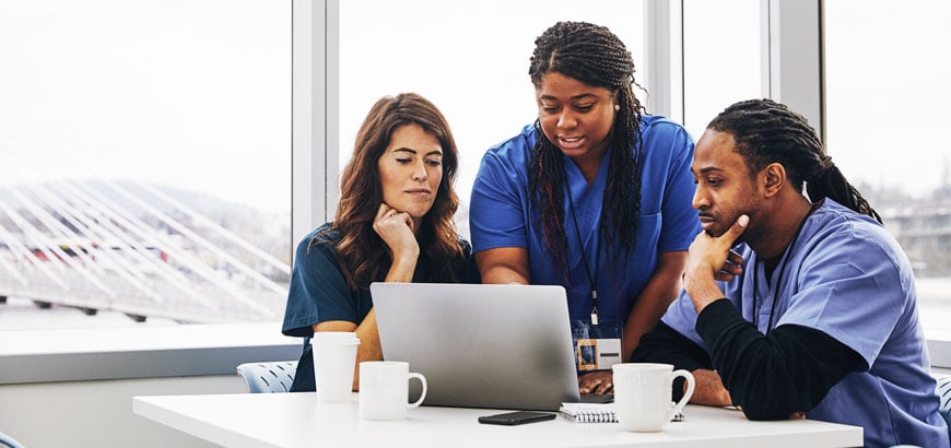 Three health professionals examine a computer screen together<br>  