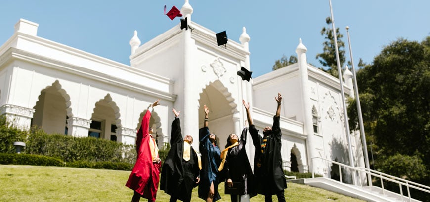 A group of people in graduation gowns toss their graduation caps into the air