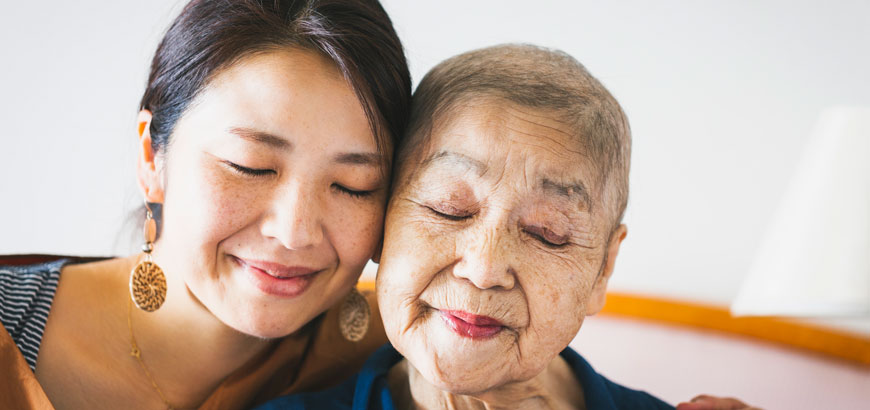 <span>Daughter in her 40's and her older mother in her 80's, whose hair is going bald since she has taken anti cancer drugs, embrace each other.</span>