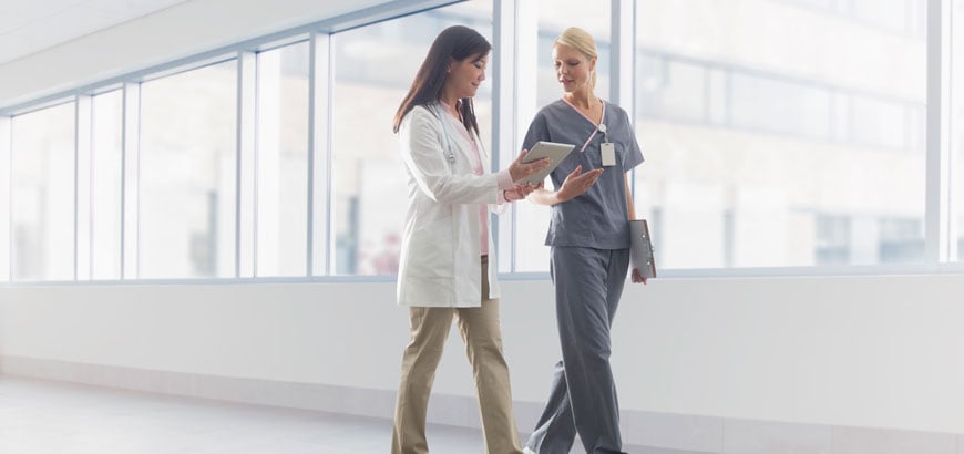 Two hospital employees walk down a hallway and have a conversation