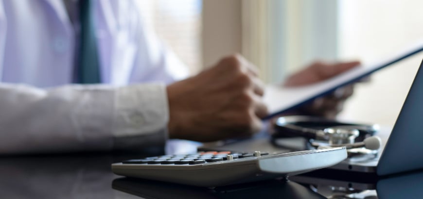 Image of doctor's hands with a calculator nearby<br>  