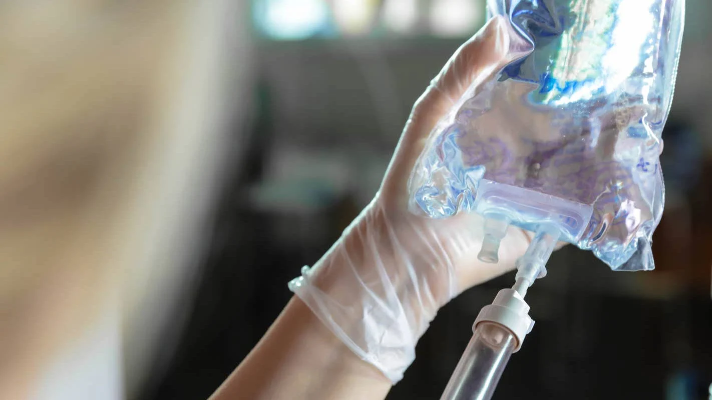 Close up of a gloved hand holding an IV bag