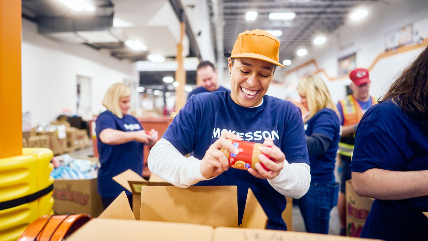 A McKesson team member happily packs a jar of peanut butter into a cardboard box for a food drive.