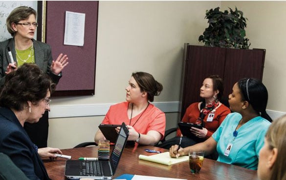 Healthcare workers sit around a conference room table and listen to a presentation.