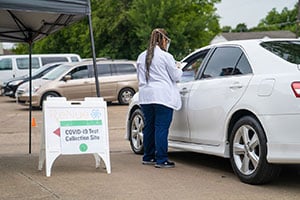 A worker talking to a person sitting in their car at a drive thru COVID-19 testing site