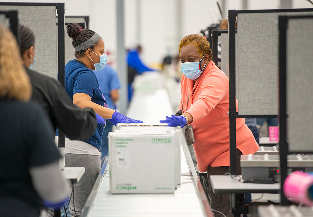 Employees pass Moderna vaccine boxes down the conveyor belt